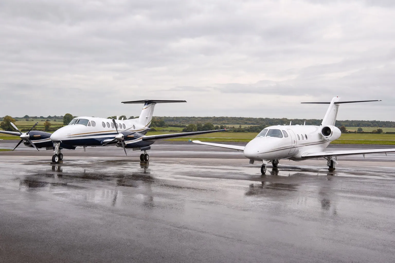 A twin-engine King Air turboprop parked beside a light business jet on the apron of a UK regional airfield